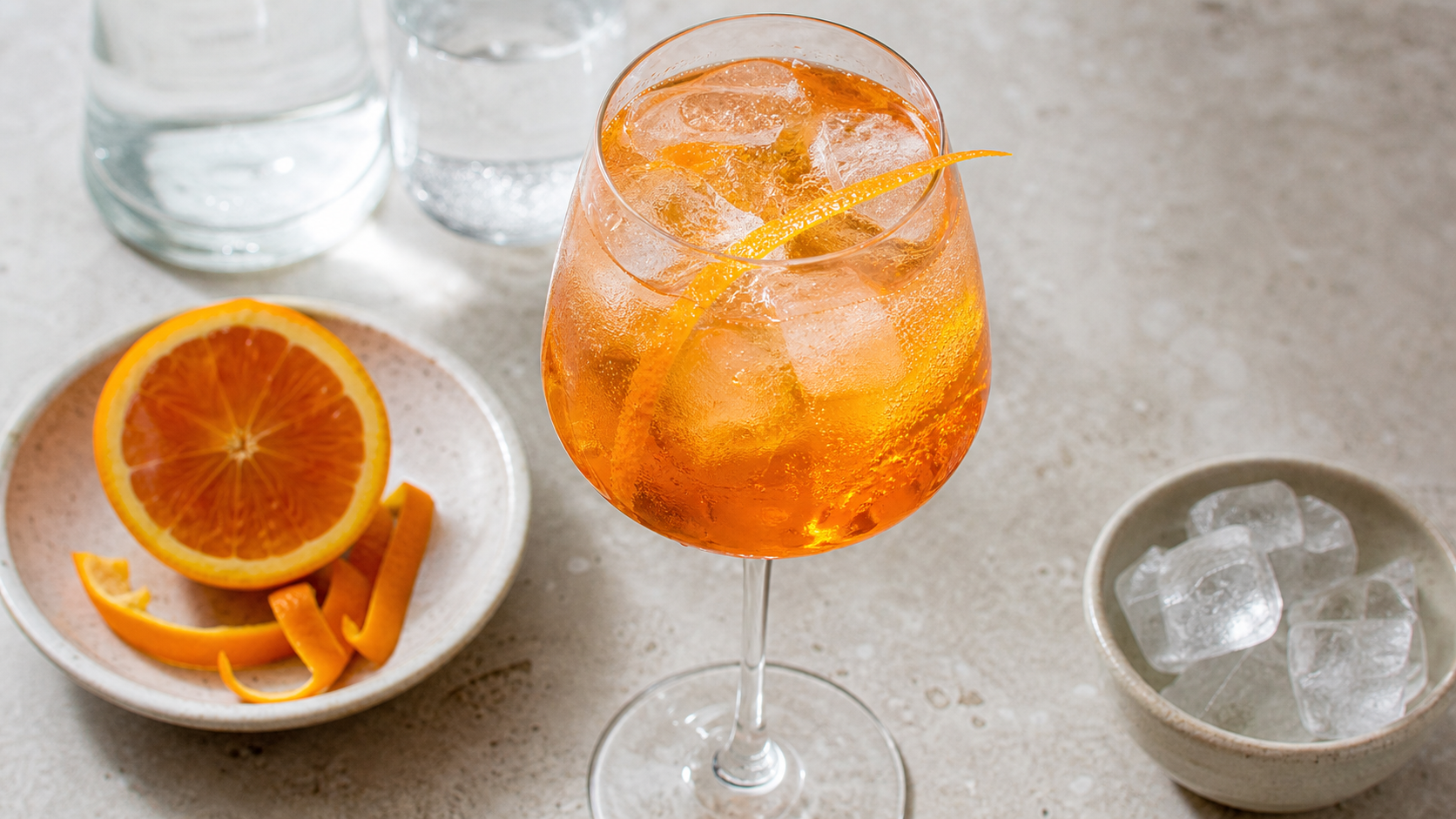Alkoholfreier Keto-Aperitif in einem Weinglas auf Eis, orange-bernsteinfarben, mit Orangenzeste garniert