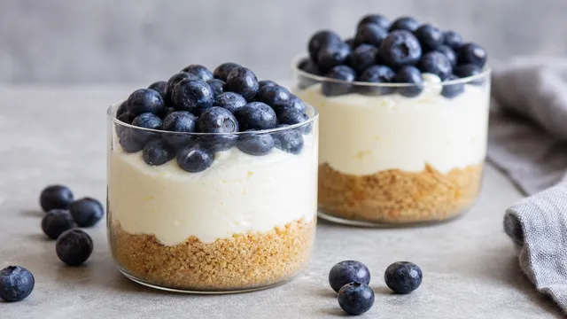 Cremiger Keto-Käsekuchen im Glas mit Mandelboden, Frischkäsecreme und frischen Blaubeeren obenauf