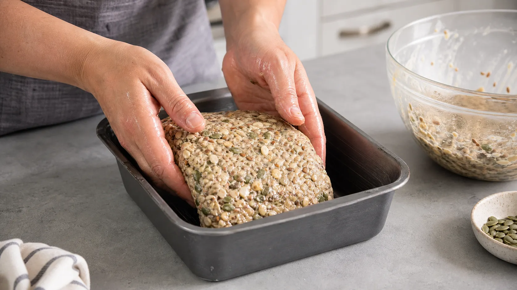 Keto-Brotteig mit Saaten wird mit nassen Händen in eine gefettete Kastenform gesetzt