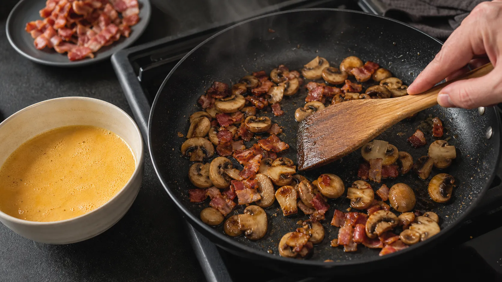 Champignons und Speck braten in der Pfanne, daneben verquirlte Eier mit Sahne