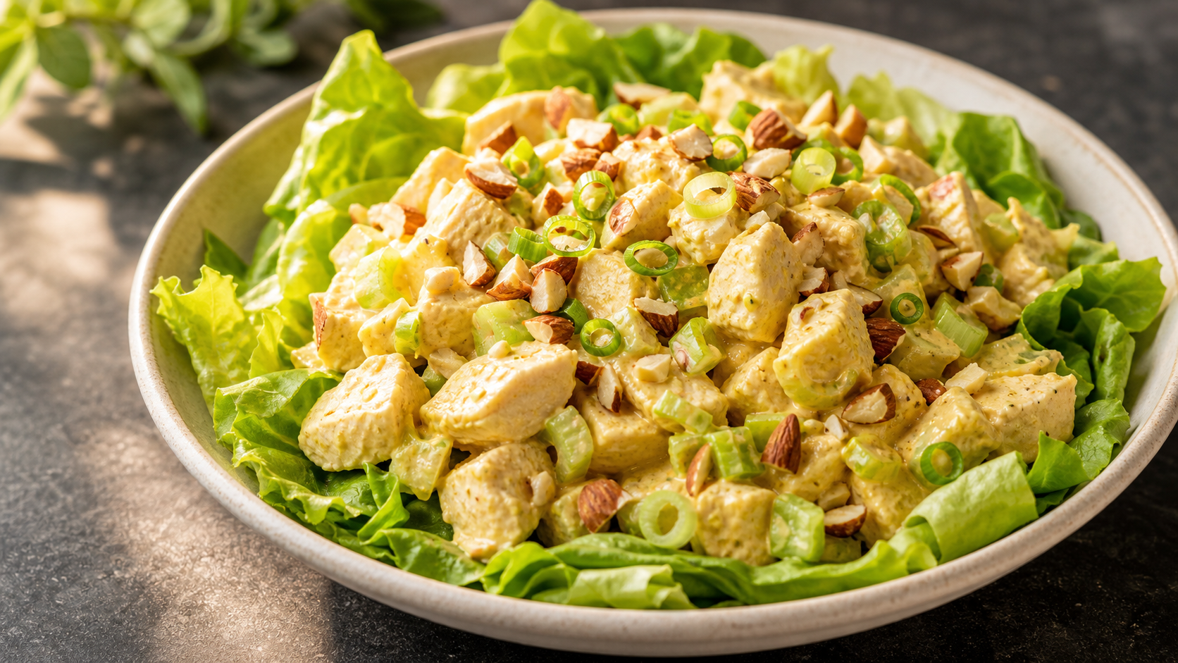 Cremiger Keto-Curry-Hähnchen-Salat mit Mandeln und Frühlingszwiebeln auf einem Salatbett angerichtet