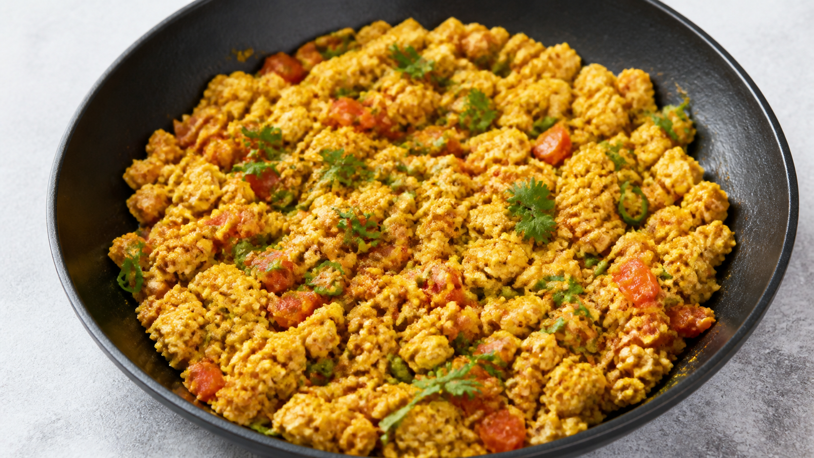 Keto-Egg-Bhurji als goldgelbes Masala-Rührei mit Tomatenstückchen, grüner Chili und frischem Koriander in einer schwarzen Pfanne
