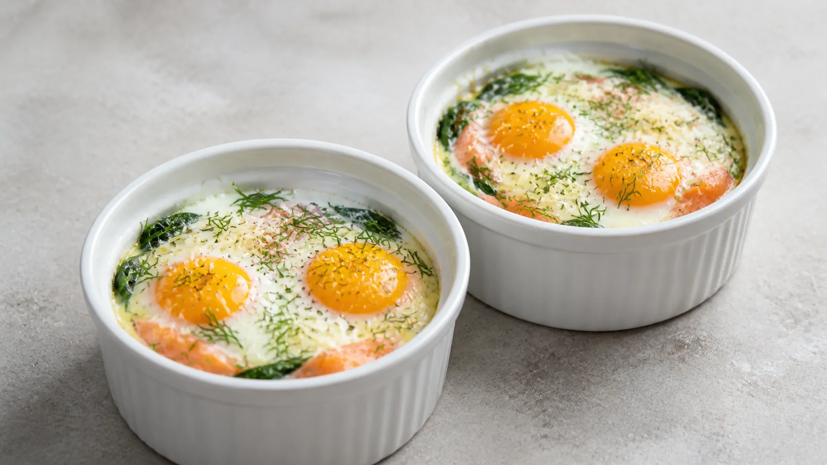 Zwei Auflaufförmchen mit Keto Eiern en Cocotte, Räucherlachs, Spinat und Sahne, bestreut mit Dill