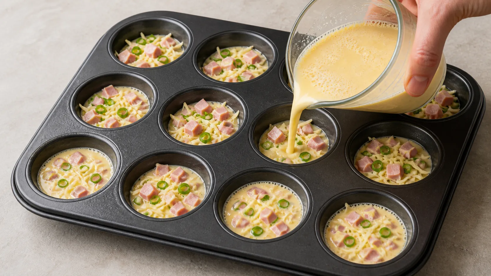 Eiermasse mit Schinken und Käse wird in die Mulden eines gefetteten Muffinblechs gefüllt