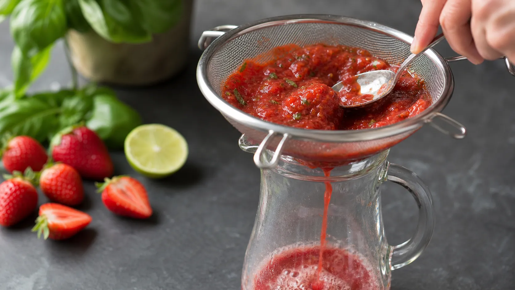 Pürierte Erdbeeren werden durch ein Sieb in eine Karaffe mit Sprudelwasser gegossen