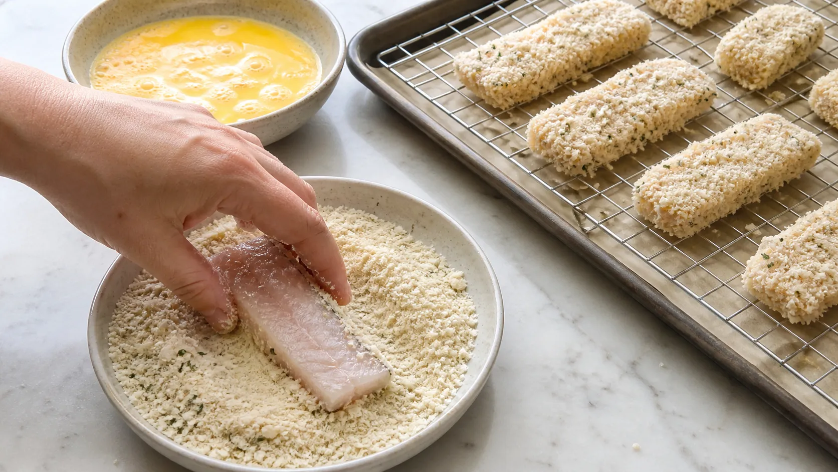 Fischstreifen werden in einer Schale mit Mandel-Parmesan-Mischung gewendet und auf ein Backblech gelegt