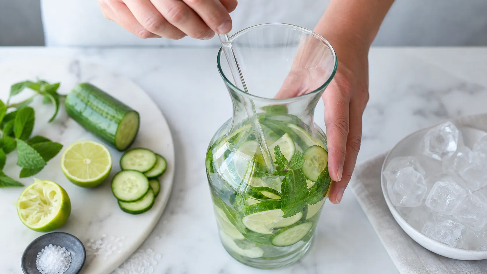 Gurkenscheiben, Limettensaft und Minze werden in einer Karaffe mit Wasser verrührt