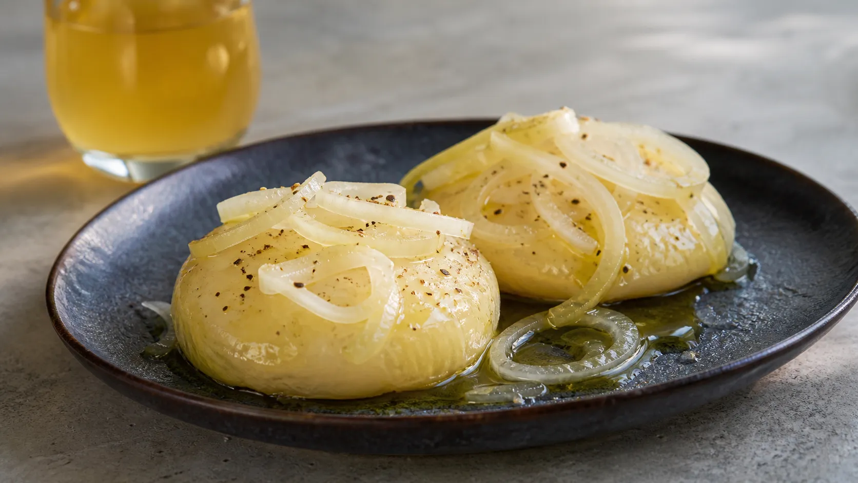 Handkäse mit Äppelwoi-Marinade auf einem Teller mit Zwiebelringen, Olivenöl und Pfeffer