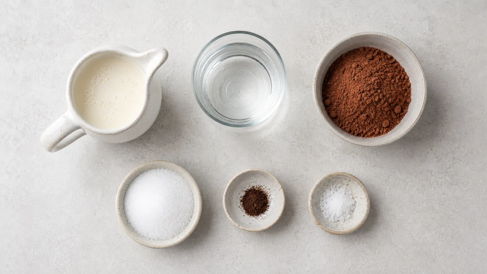Flatlay der Zutaten für Keto heiße Schokolade mit Sahne, Wasser, Backkakao, Erythrit, Vanille und Salz