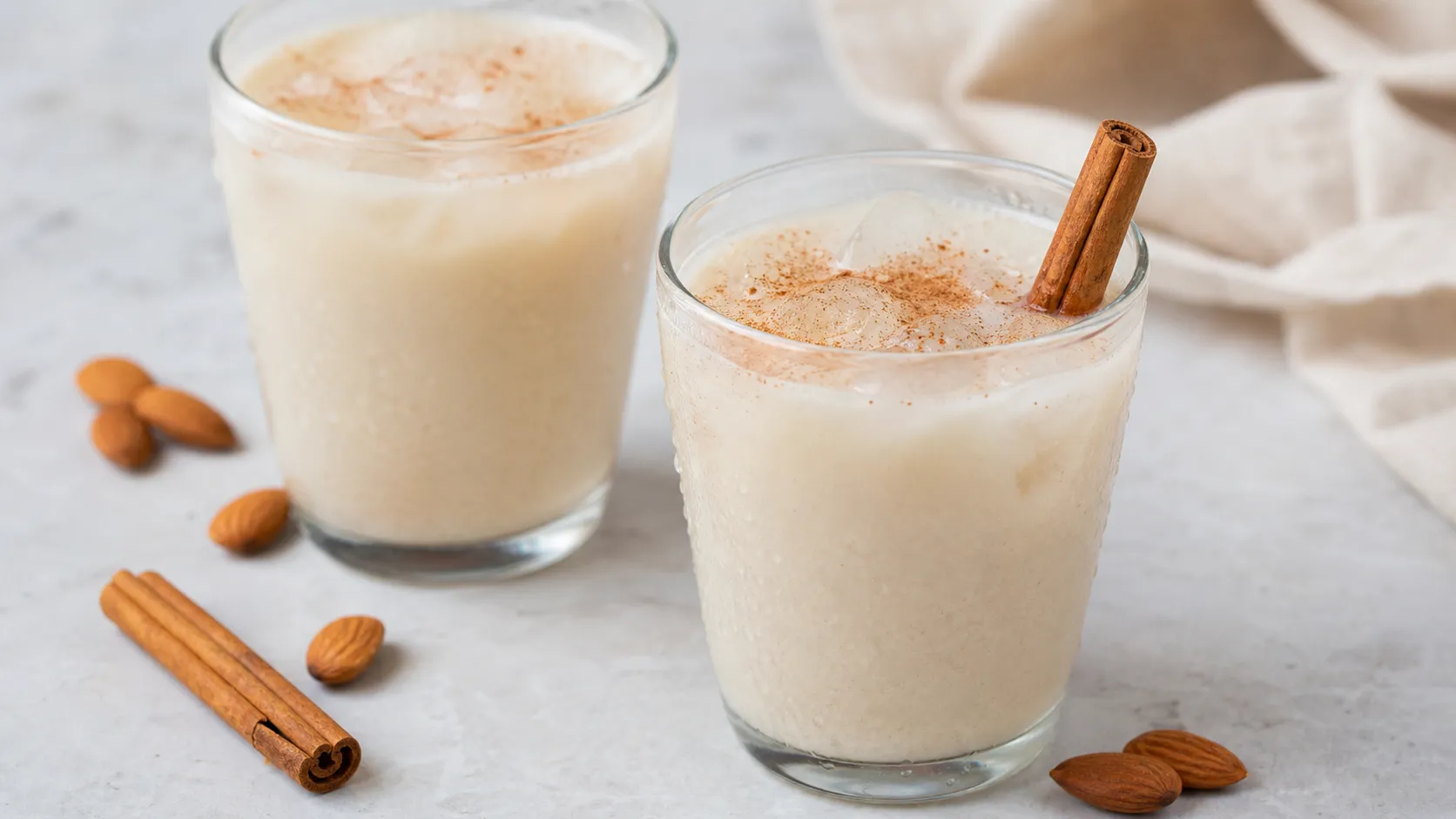 Zwei Gläser Keto-Horchata mit Eiswürfeln, Zimtstange und einer Zimtstaub-Schicht auf der Oberfläche