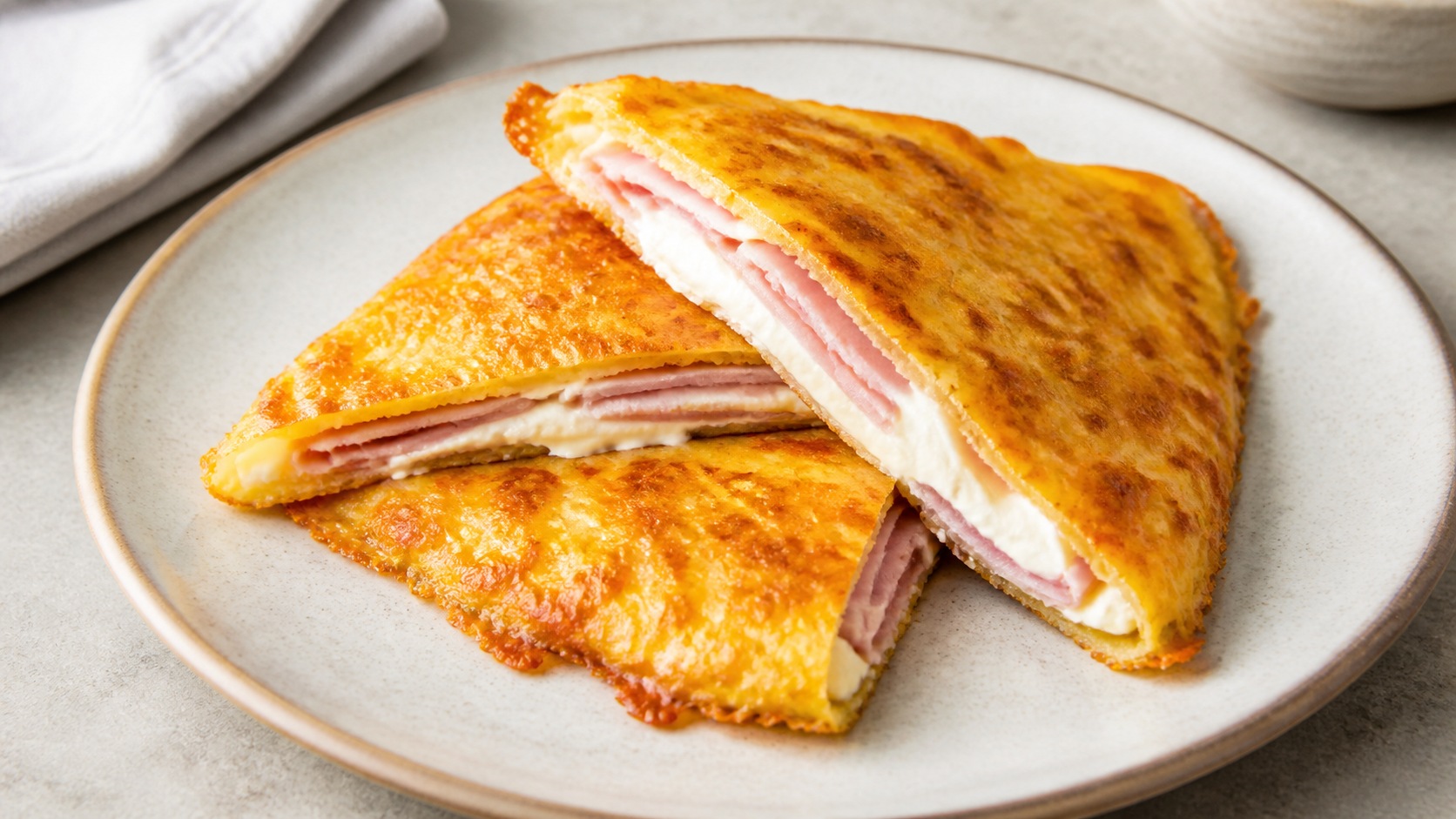 Zusammengeklappte Keto-Käse-Quesadilla mit Schinken und Frischkäse, in Spalten geschnitten auf einem Teller