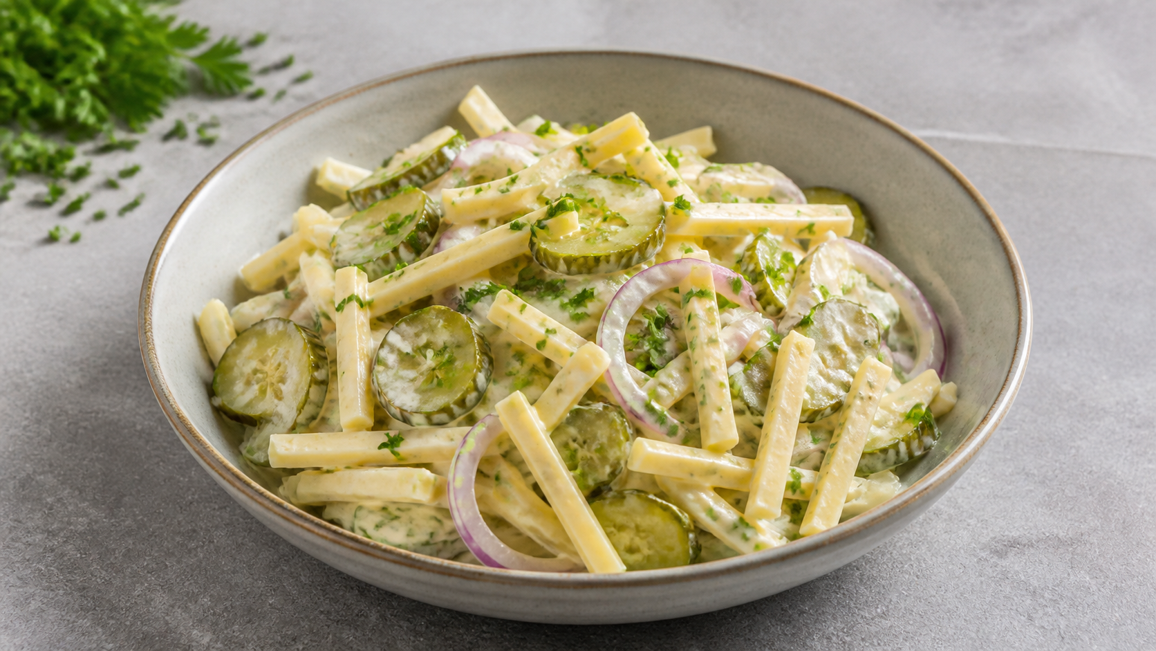 Keto-Käsesalat mit Emmentaler-Streifen, Gewürzgurken, roter Zwiebel und Schnittlauch in einer Schüssel