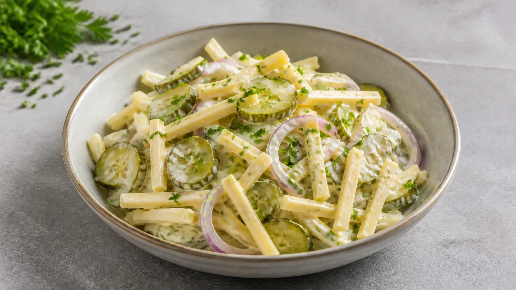 Keto-Käsesalat mit Emmentaler-Streifen, Gewürzgurken, roter Zwiebel und Schnittlauch in einer Schüssel