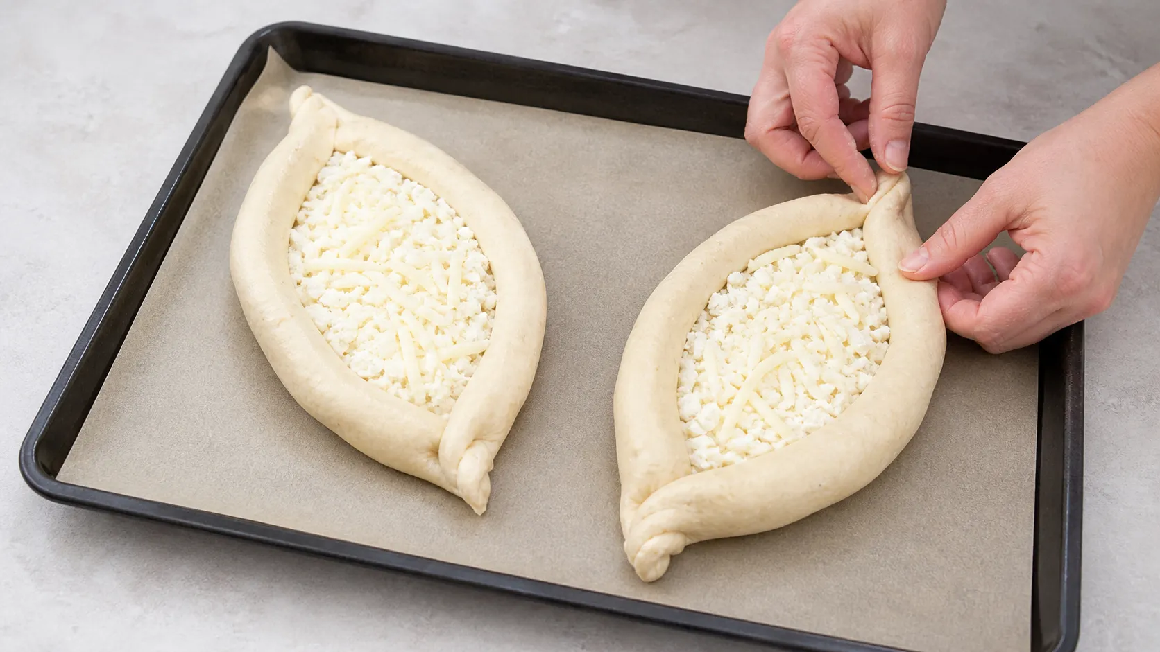 Zwei geformte Teigboote aus Mandelmehl-Käseteig auf einem Blech, gefüllt mit Käsemischung vor dem Backen