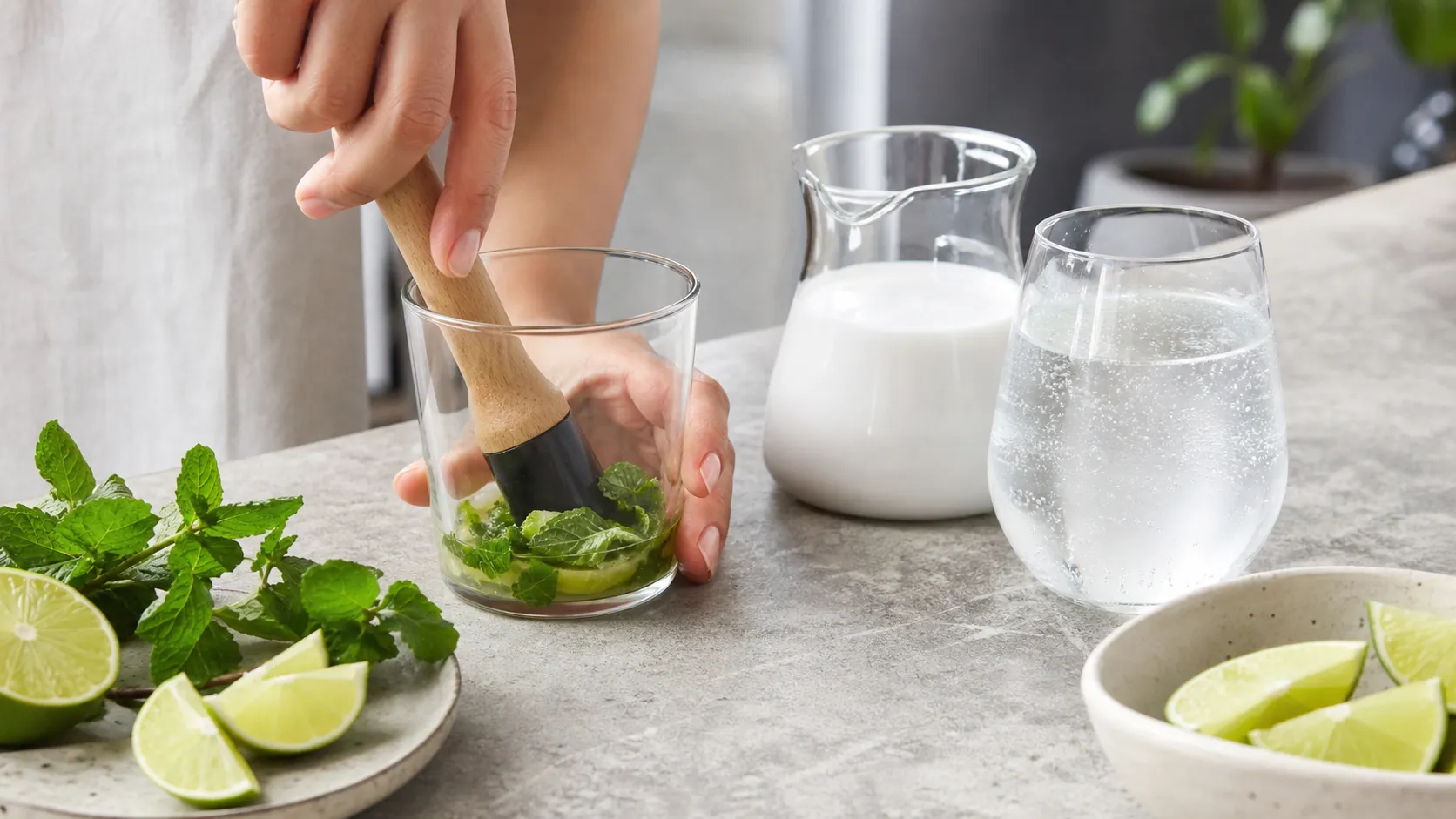 Minzblätter werden mit Limettensaft und Erythrit im Glas angedrückt, daneben steht die Kokosmilch