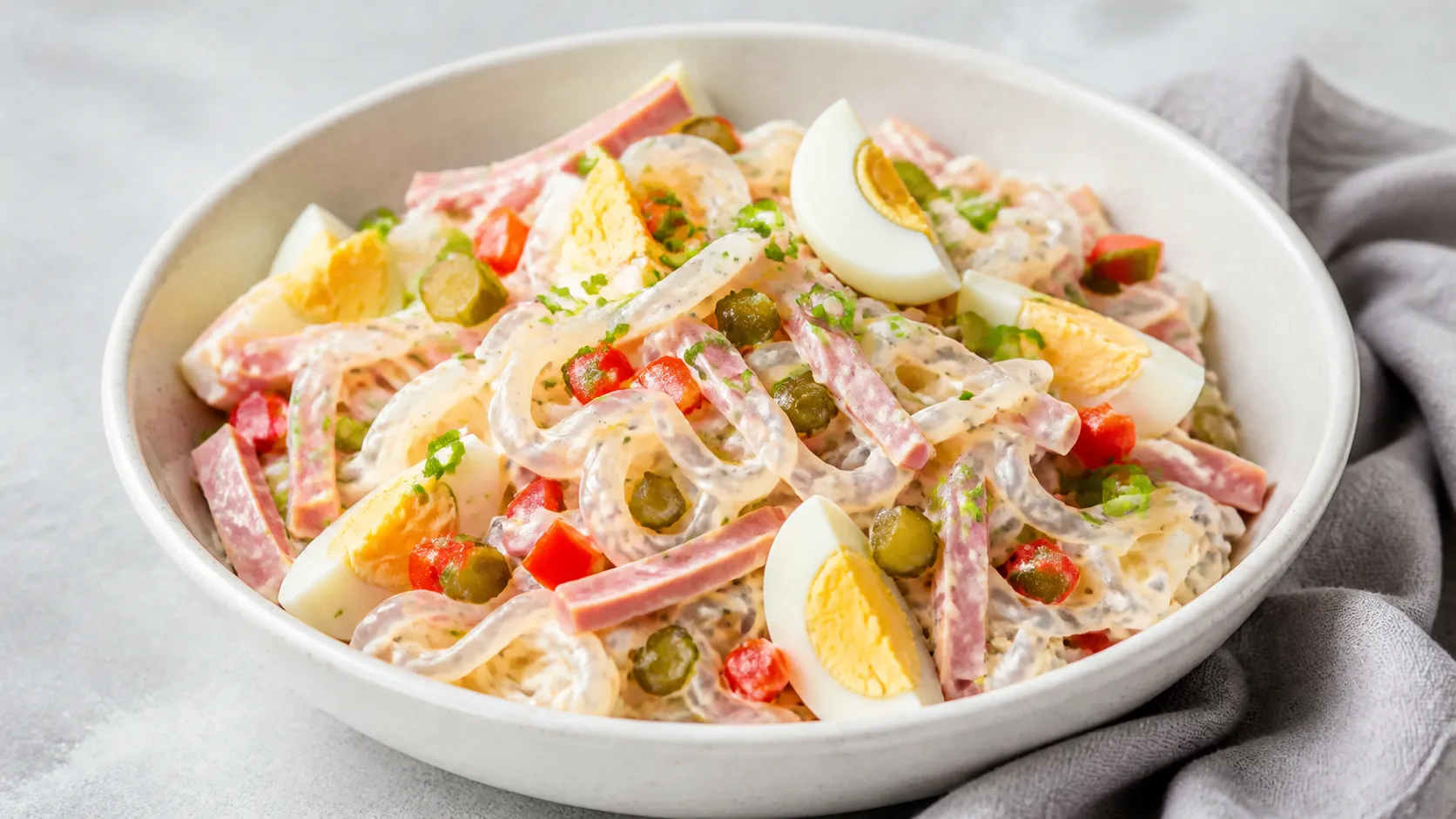 Schüssel mit Keto Konjak-Nudelsalat, Schinkenstreifen, roter Paprika, Ei-Vierteln und Petersilie