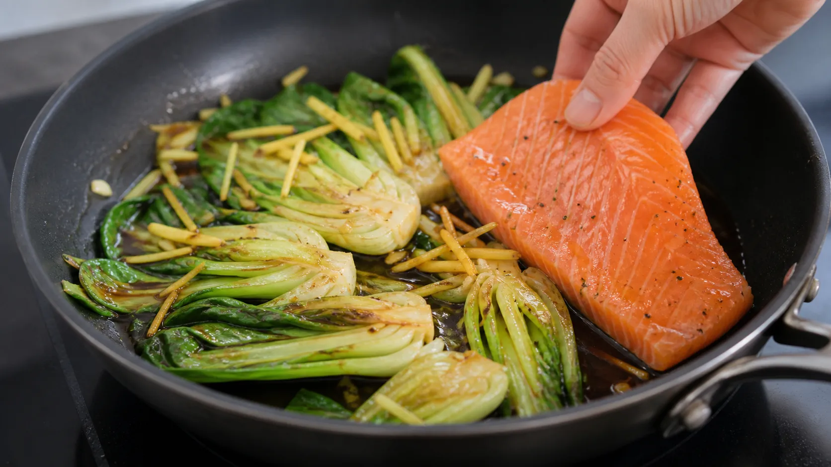Pak Choi und Ingwer braten in Sesamöl, während Lachsfilet in der Pfanne gegart wird