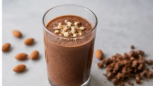 Keto-Mandelbutter-Kakao-Smoothie im Glas mit gehackten Mandeln und Kakaopulver