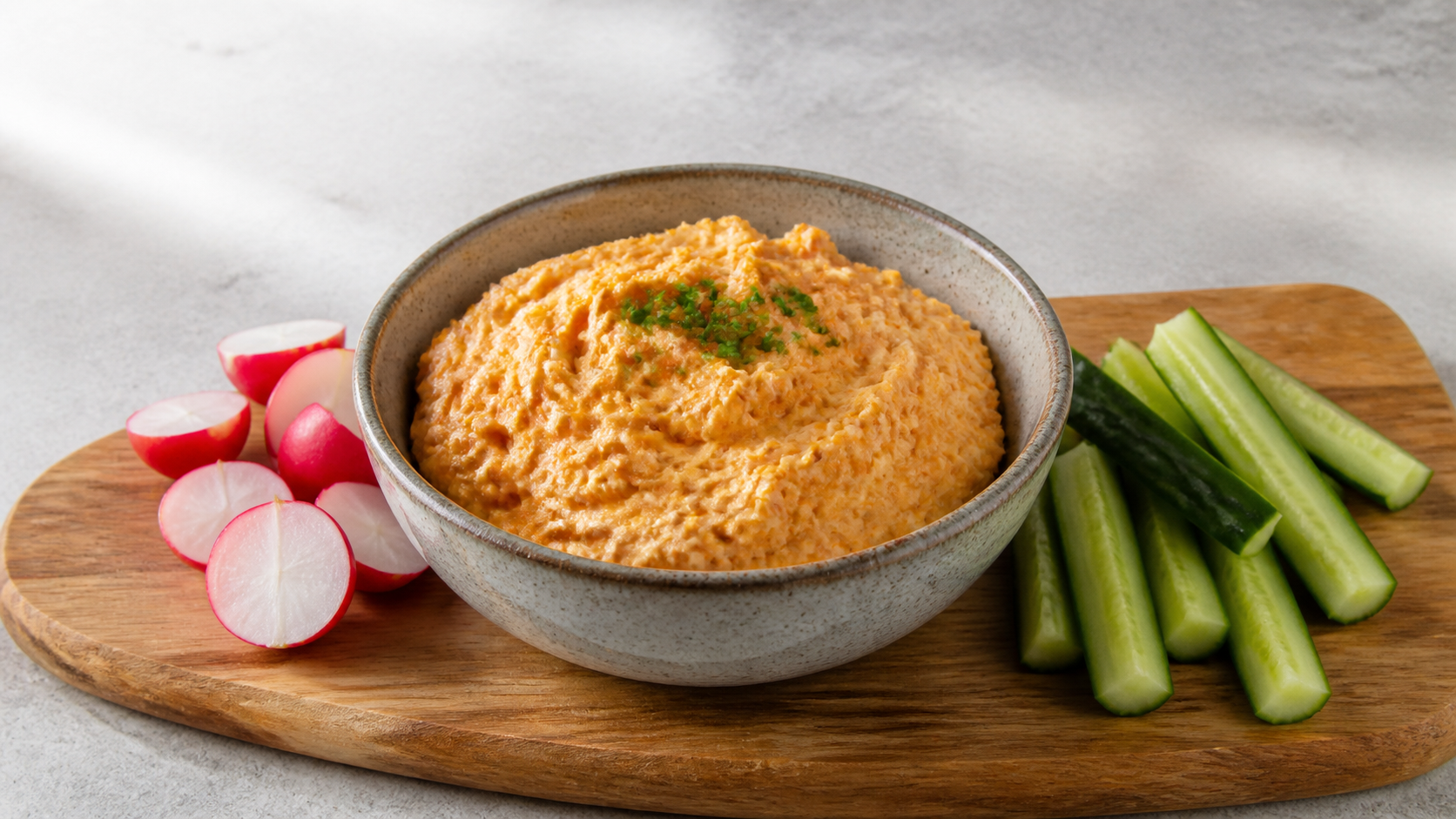 Keto-Obatzda in einer Schale mit Radieschen, Gurkensticks und Schnittlauch auf einem Holzbrett