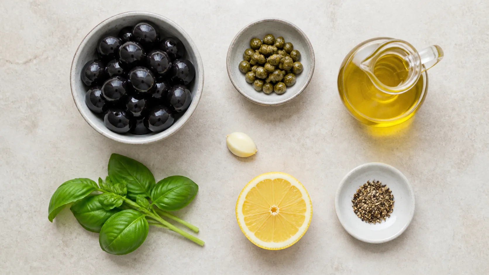 Zutaten für Keto-Tapenade: schwarze Oliven, Kapern, Knoblauchzehe, Basilikum, Olivenöl und Zitrone