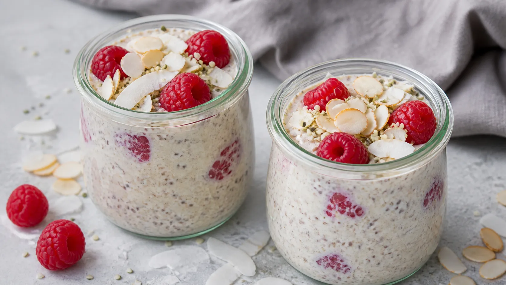 Zwei Gläser Keto Overnight-Müsli mit Hanfsamen, Kokosraspeln, gehobelten Mandeln und frischen Himbeeren