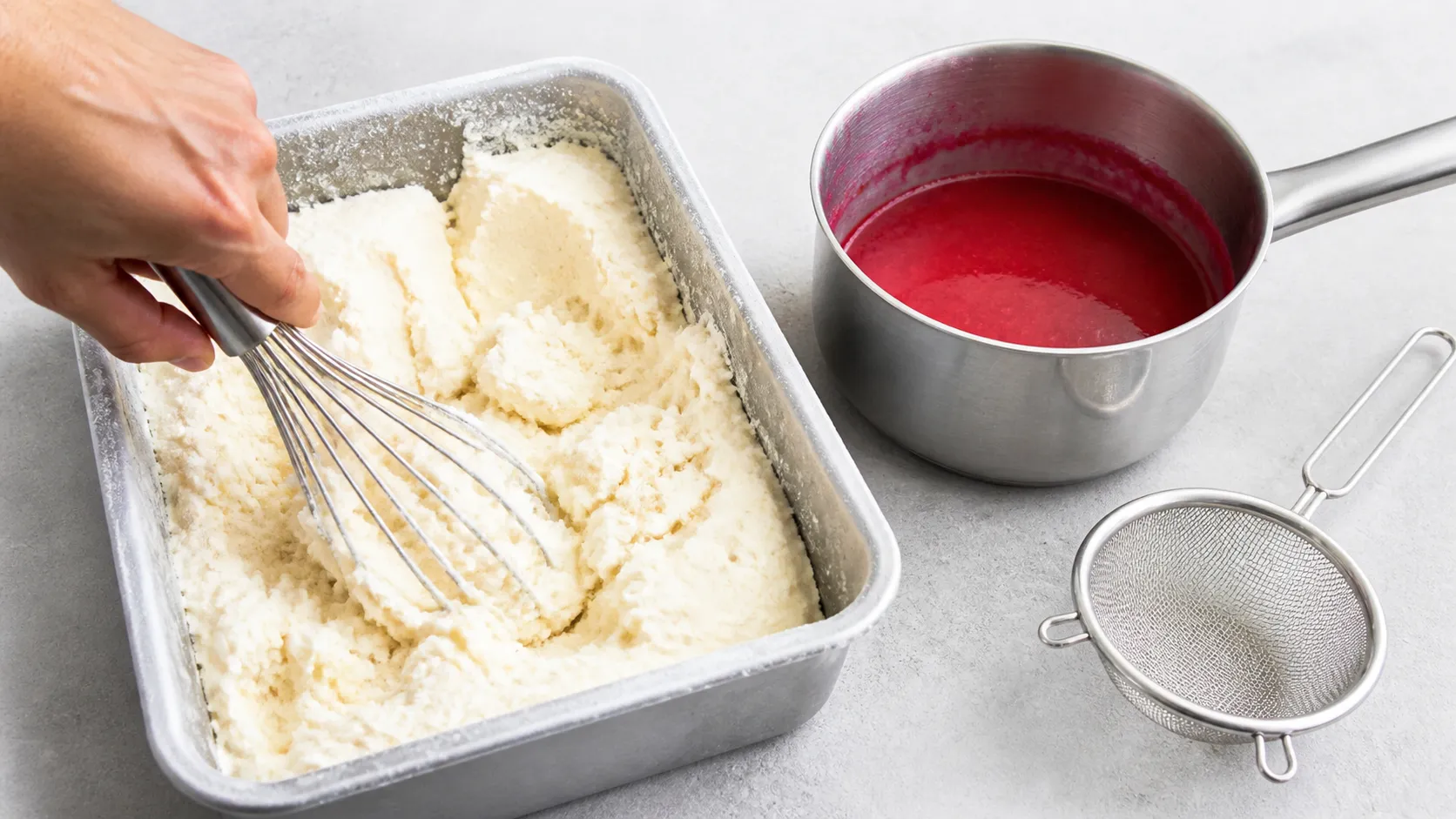 Halb gefrorene Vanilleeismasse für Keto-Pfirsich Melba wird in einer Metallform aufgeschlagen, daneben steht passierte Himbeersauce