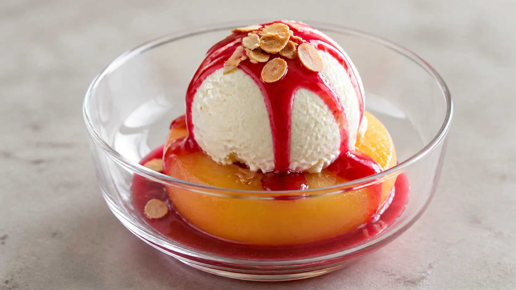 Keto-Pfirsich Melba in einer Glasschale: Pfirsichhälfte mit Vanilleeis, roter Himbeersauce und Mandelblättchen