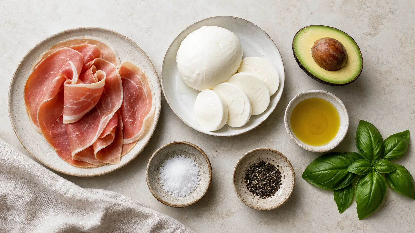 Zutaten für Keto-Frühstücksteller mit Prosciutto, Mozzarella, Avocado, Olivenöl und Basilikum