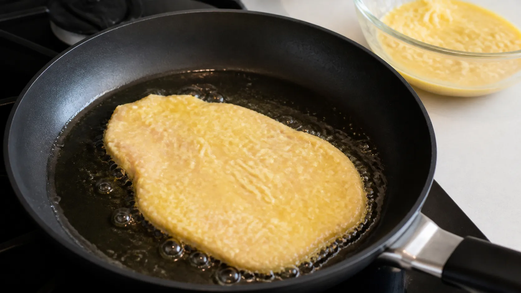 Ein in Ei-Parmesan-Masse gewendetes Putenschnitzel brät in einer Pfanne mit Olivenöl goldgelb