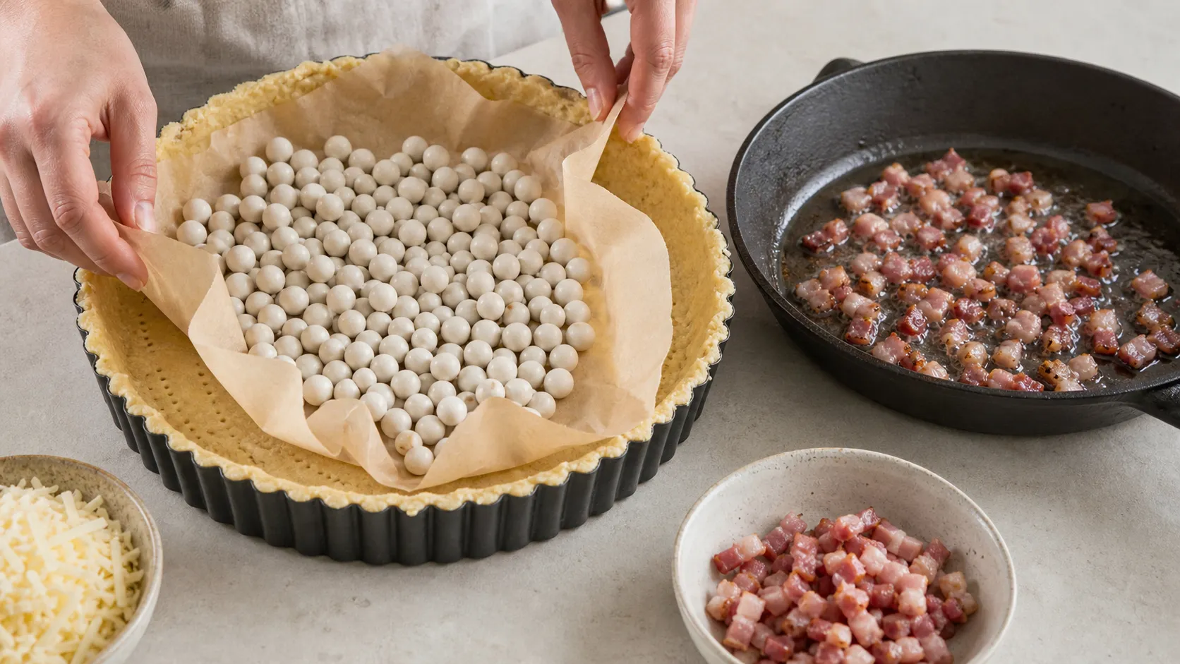 Mandelmehlboden in einer Tarteform, blindgebacken, daneben die Speckwürfel in der Pfanne