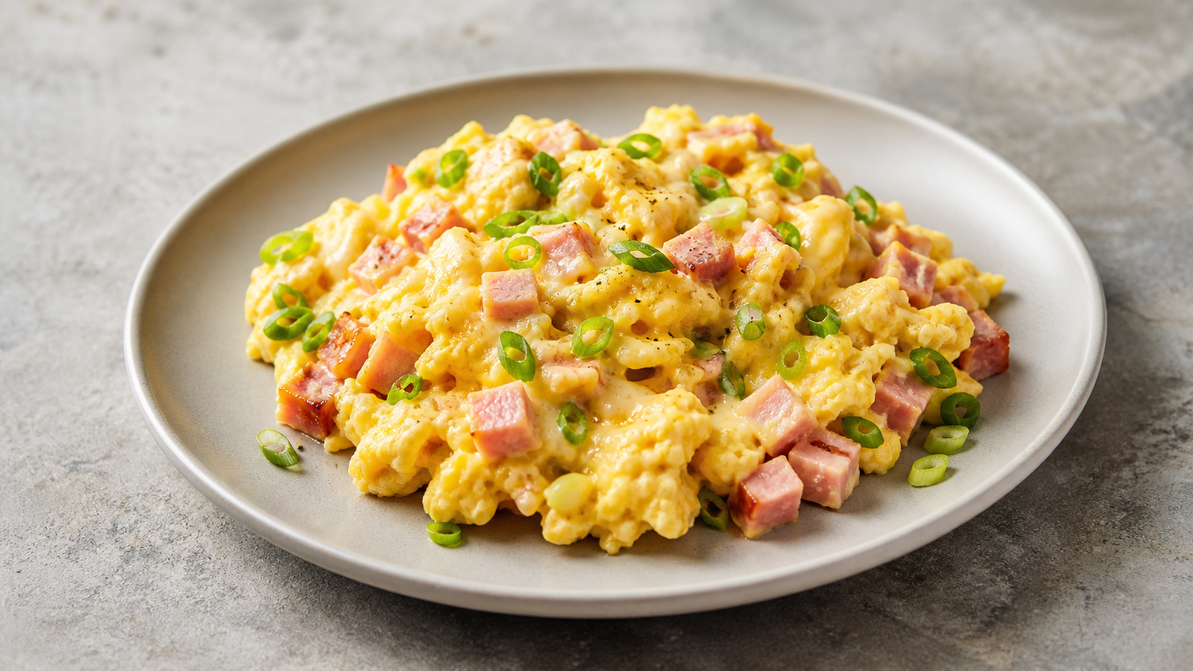 Cremiges Keto-Rührei mit Würfeln von Kochschinken, Frühlingszwiebeln und geschmolzenem Gouda auf einem Teller
