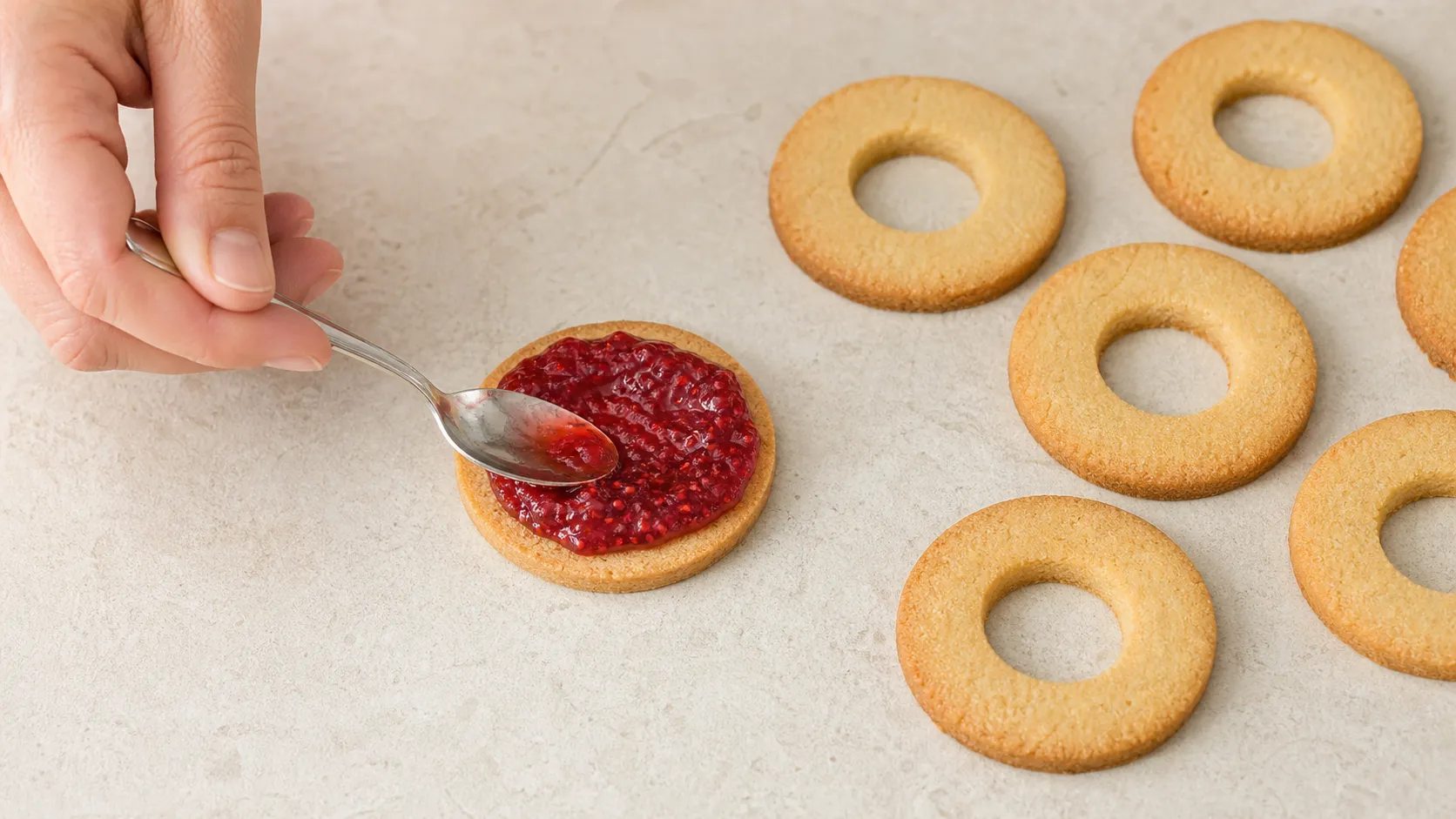Ausgestochene Plätzchenböden mit Loch werden mit Himbeer-Chia-Marmelade zusammengesetzt