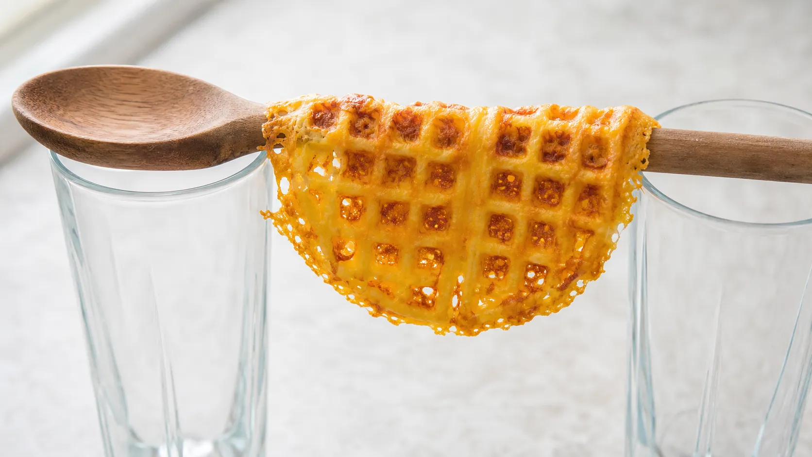 Eine warme Käsewaffel wird über einen Kochlöffelstiel gehängt, um die Taco-Form zu bekommen