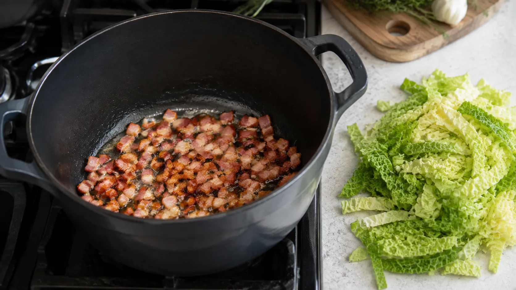 Speckwürfel braten knusprig in einem Topf aus, daneben liegen grob geschnittene Wirsingblätter
