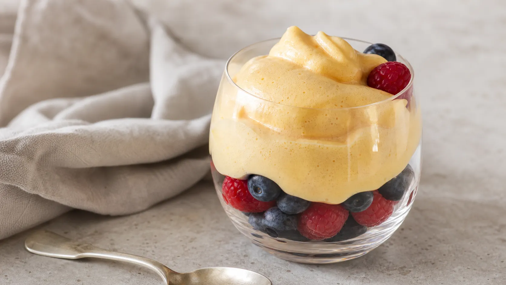Warme Keto-Zabaione als goldgelbe Schaumcreme über frischen Himbeeren und Heidelbeeren im Glas