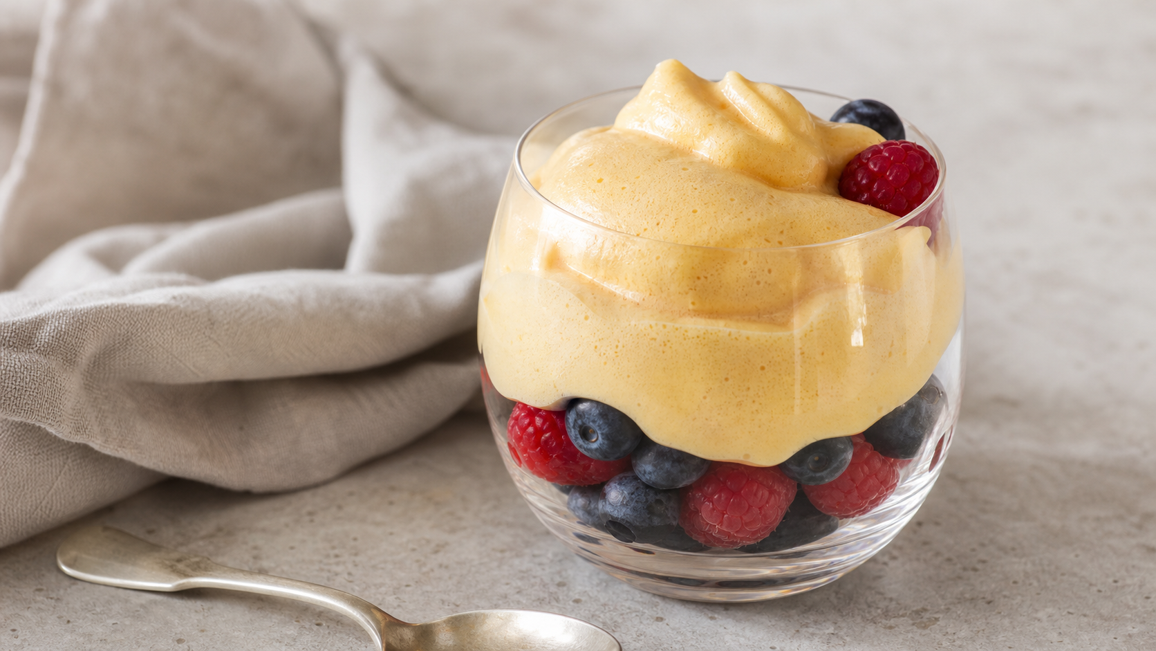 Warme Keto-Zabaione als goldgelbe Schaumcreme über frischen Himbeeren und Heidelbeeren im Glas