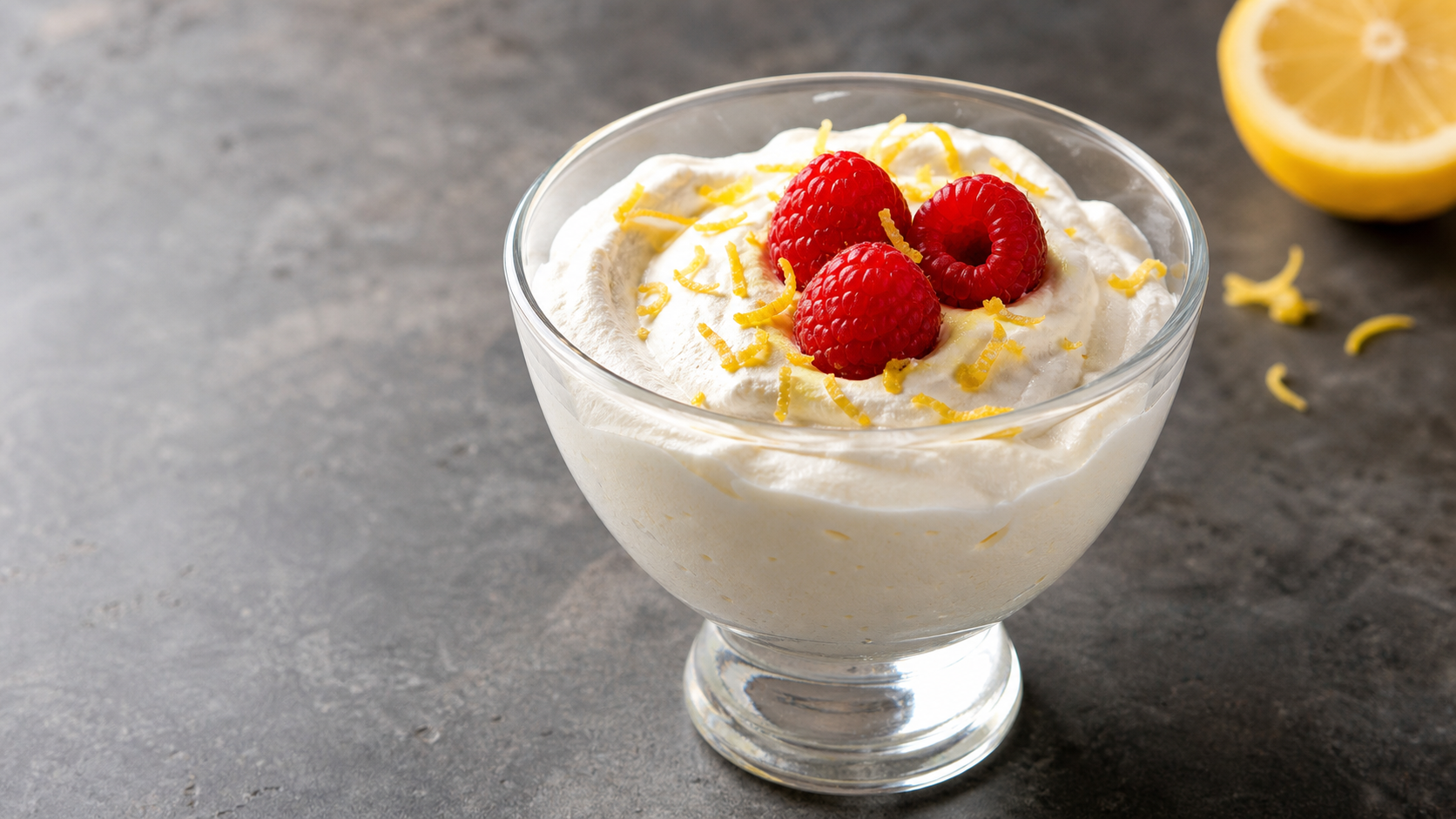 Luftige Keto-Zitronen-Quark-Mousse in einem Glas, garniert mit Himbeeren und Zitronenschale
