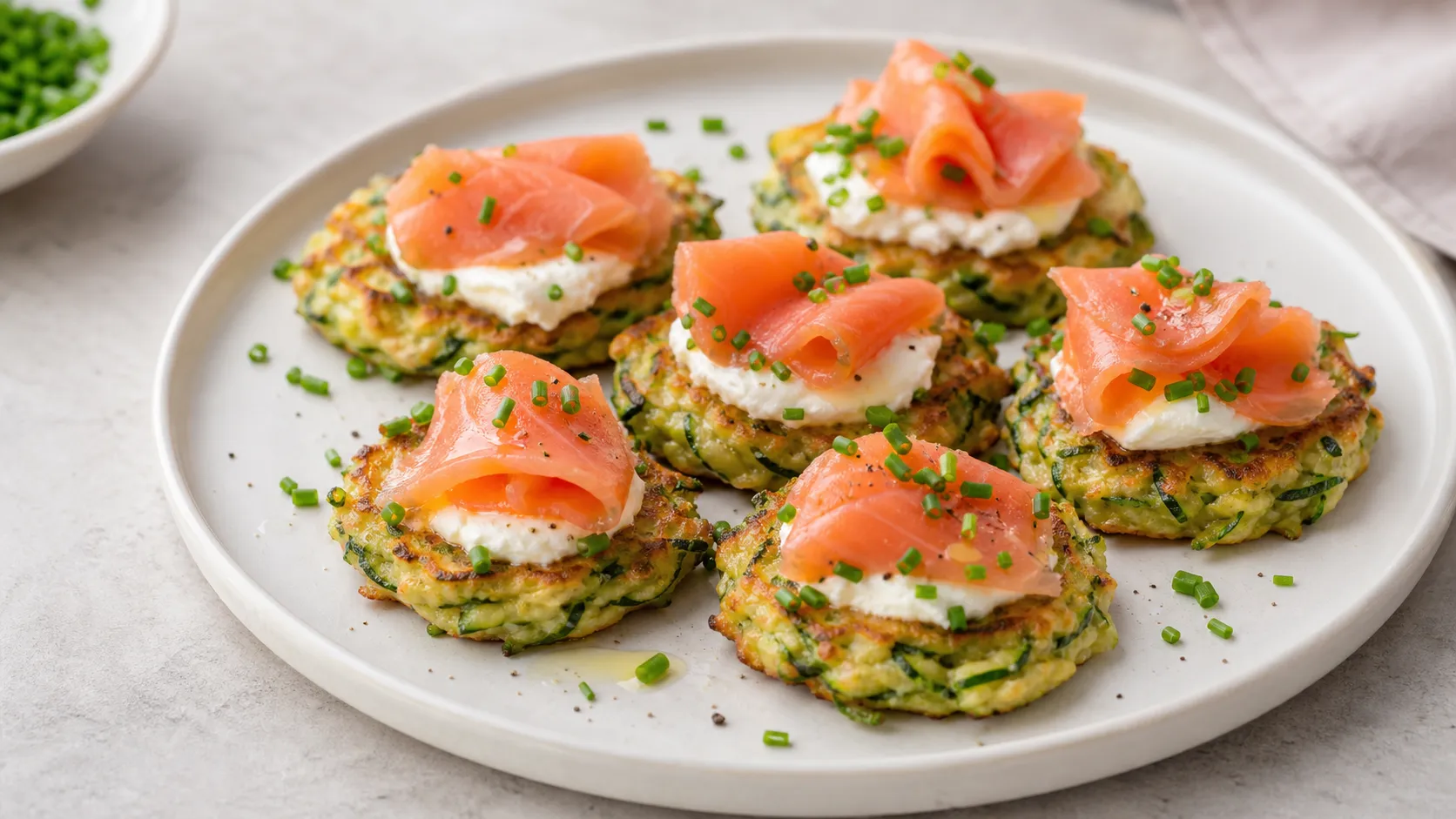 Goldbraune Keto-Zucchini-Puffer mit Frischkäse, Räucherlachs und Schnittlauch auf einem Teller