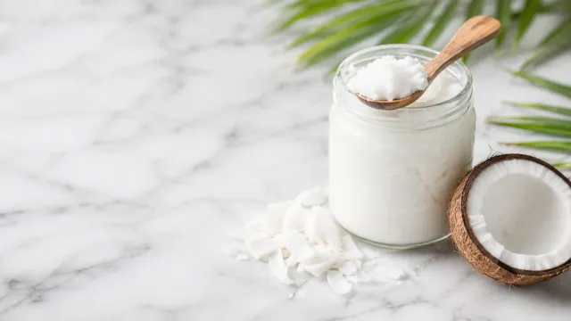 Keto Lebensmittel: Glas mit weißem nativem Kokosöl, daneben eine halbierte Kokosnuss und ein Löffel